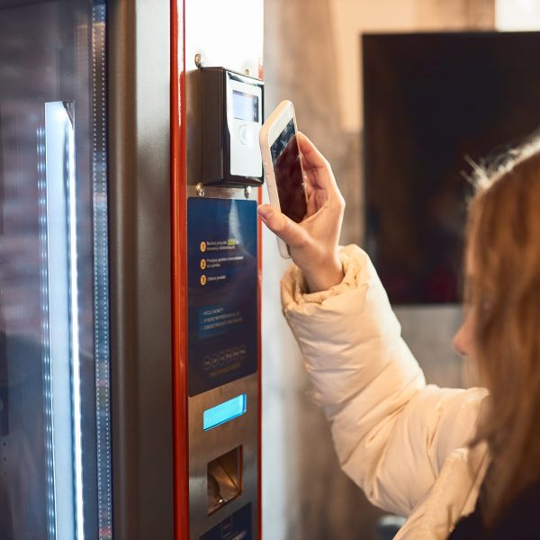 Woman paying for product at vending machine using contactless method of payment with mobile phone. Woman using new way of payments